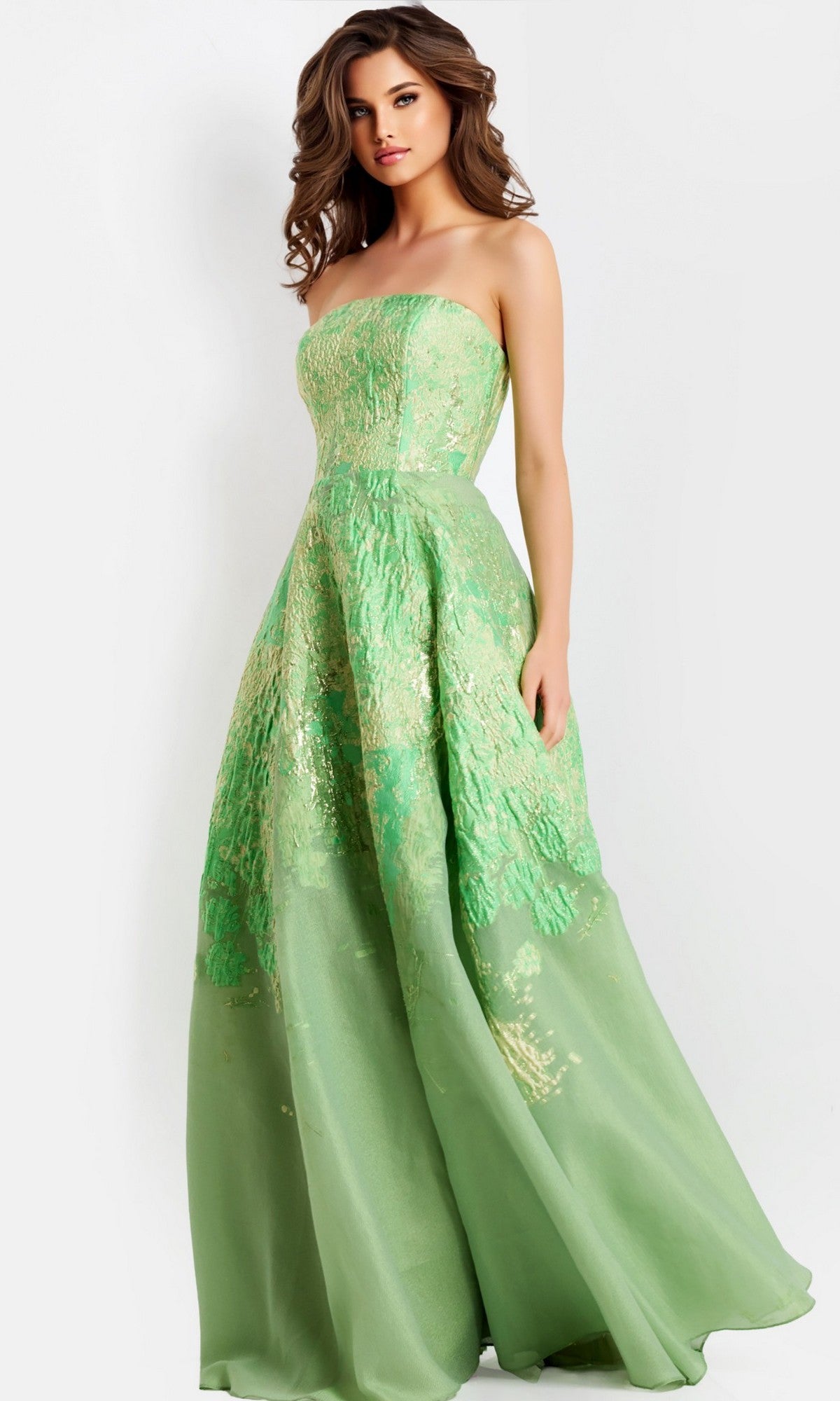 A woman wears the Long Prom Dress: Jovani 46260 in light green, featuring a strapless fitted bodice, elegant A-line skirt, and metallic accents, standing against a plain light background.